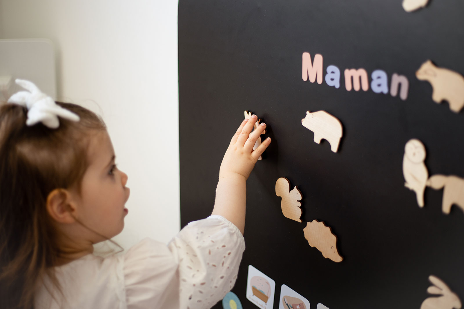 Petite fille jouant avec des magnets en bois sur un papier peint magnétique
